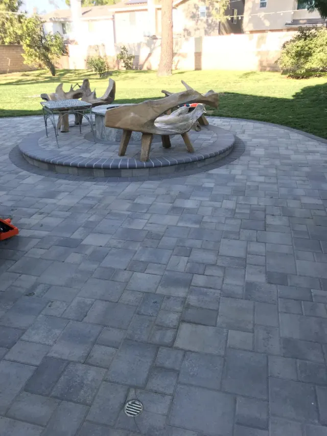 Outdoor kitchen, pavers and patio cover: a gray paver patio around a round fire pit area with log seating