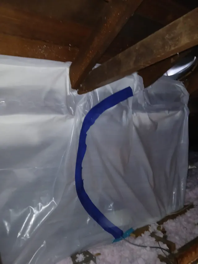 White plastic sheeting taped up in an attic beside the rafters and insulation during a repair