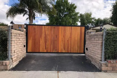 Wood driveway gate in a black steel frame between brick pillars